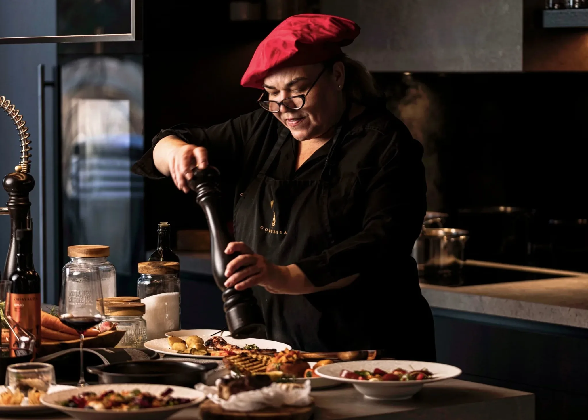 The private chef in a red beret grinding pepper over a course at the table